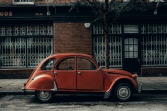 An old red car parked in front of a building