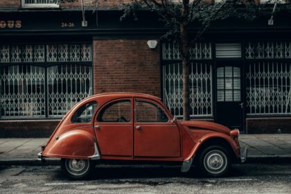 An old red car parked in front of a building