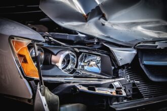 A damaged silver car with a crushed hood and broken headlight assembly
