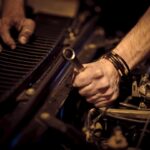 Hands with grease working on a car engine with a metal wrench