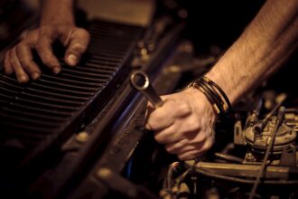 Hands with grease working on a car engine with a metal wrench