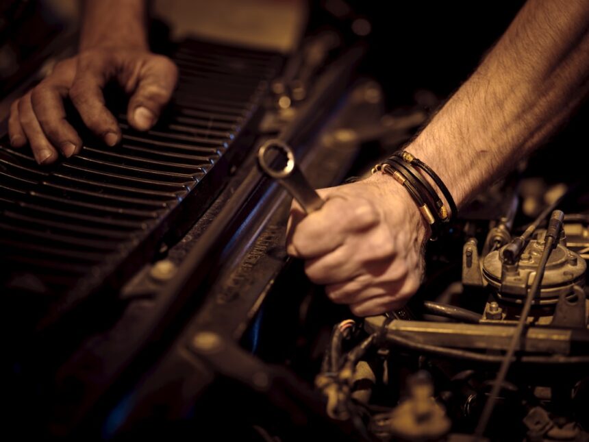 Hands with grease working on a car engine with a metal wrench