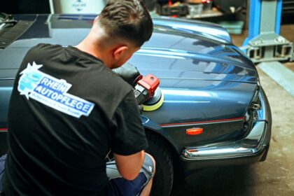 A person polishing a blue vintage car in a workshop