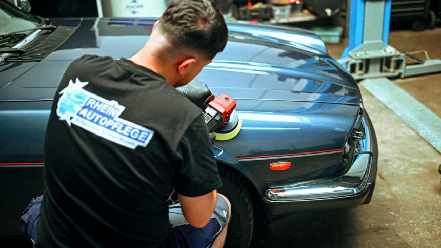A person polishing a blue vintage car in a workshop