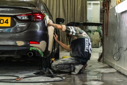 A person sanding the rear bumper of a grey car in a workshop