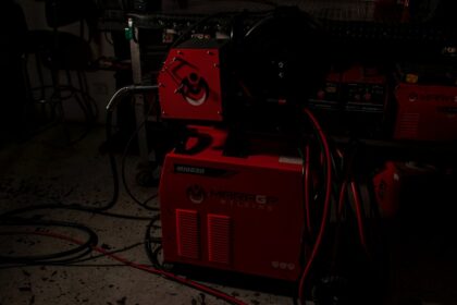 A red welding machine with cables in a dark workshop