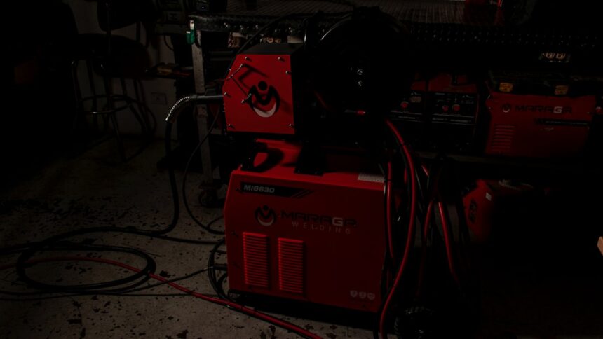 A red welding machine with cables in a dark workshop