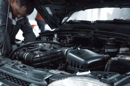 A mechanic in a grey uniform inspecting the engine of a car