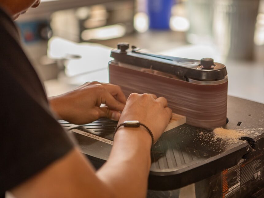 Hands sanding wood on a belt sander
