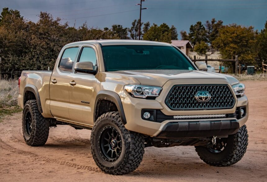 A tan Toyota Tacoma pickup truck on a dirt road with black wheels