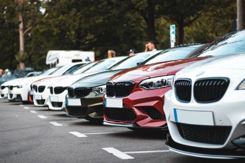 A row of parked cars including white, olive, and red sedans in a lot