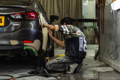 A person sanding the rear panel of a grey car in a workshop