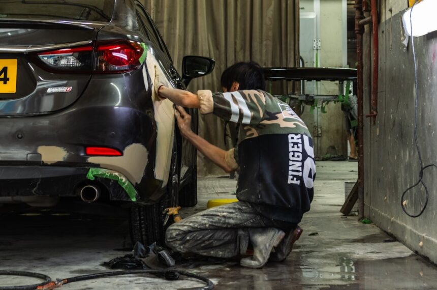 A person sanding the rear panel of a grey car in a workshop