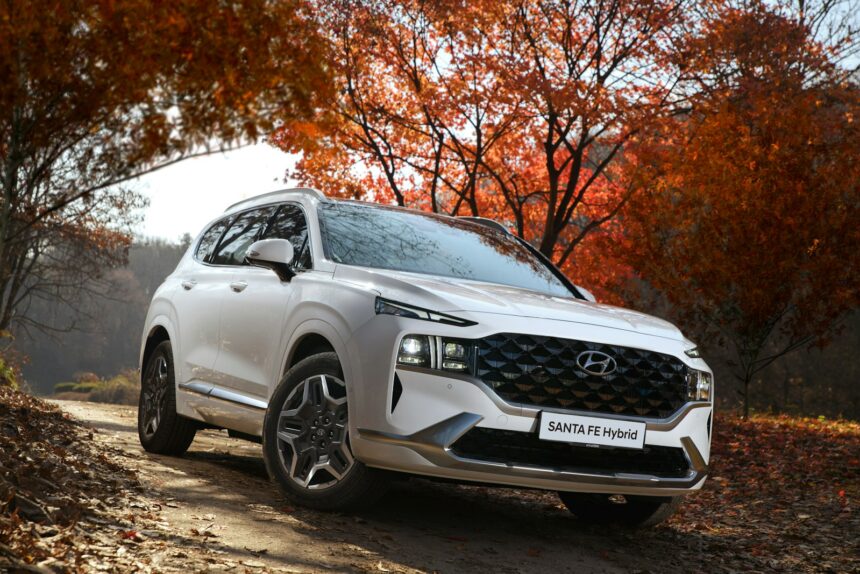 White Hyundai Santa Fe parked on a road lined with autumn trees